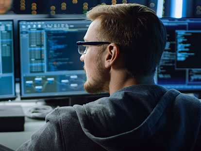Man with hoodie and glasses staring at computer monitor